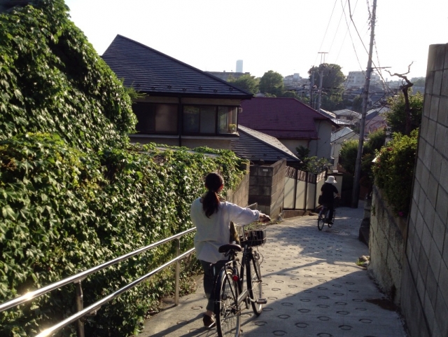 坂道を自転車を押して歩く女性